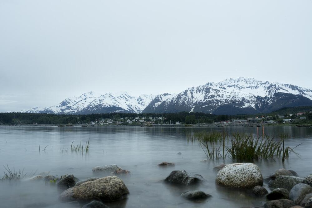 Body of water before mountains and town with cloudy skies