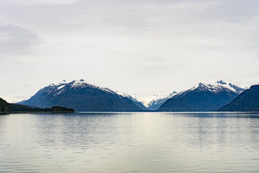 Body of water before two mountains with cloudy skies Body of water before two mountains with cloudy skies