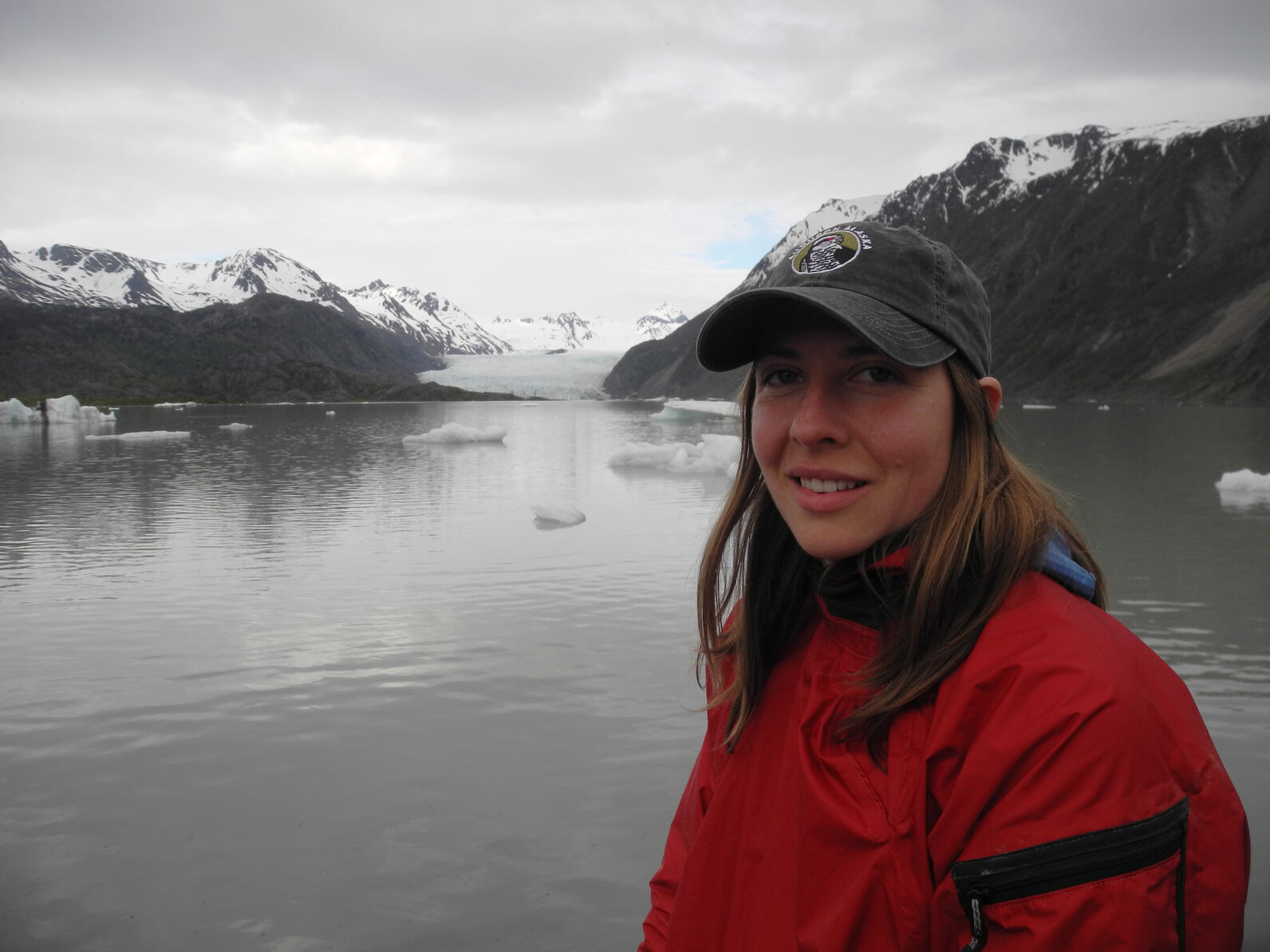 Woman in hat standing in front of water and glacier